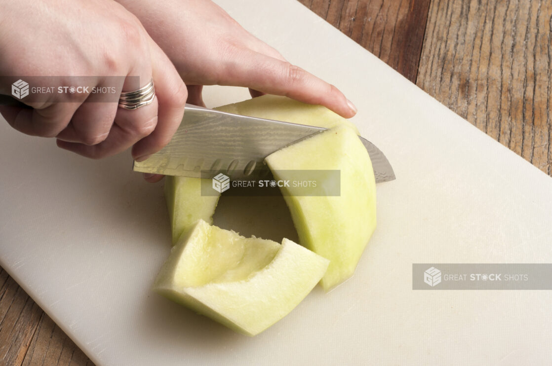 Hands cutting melon on a white cutting board on a rustic wooden table, close-up