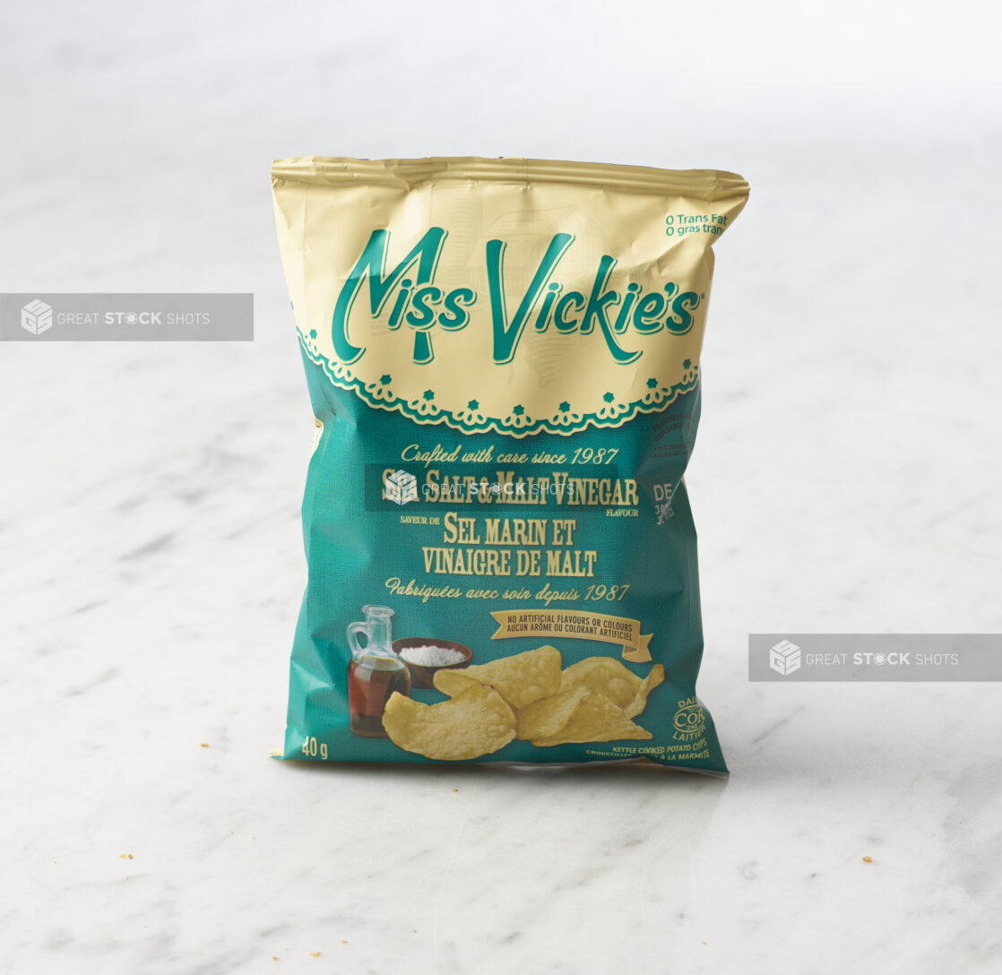 Individual bag of Miss Vickie's salt and malt vinegar chips on marble background