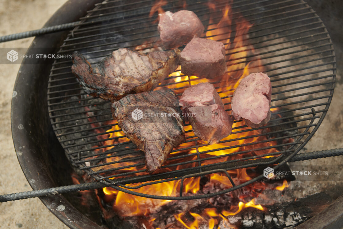 T-bone steak and Steak Medallions Grilling Over an Open Flame Barbecue in an Outdoor Setting