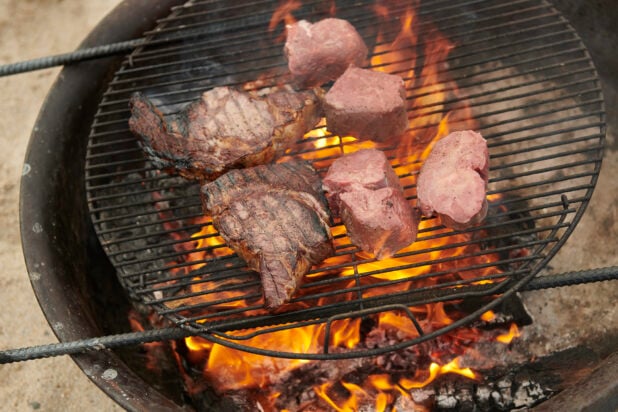 T-bone steak and Steak Medallions Grilling Over an Open Flame Barbecue in an Outdoor Setting