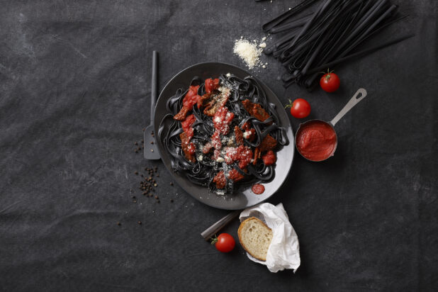 Overhead View of Black Squid Ink Fettuccine Pasta with Sun-dried Tomatoes, Marinara and Grated Parmesan Cheese on a Black Cloth Surface