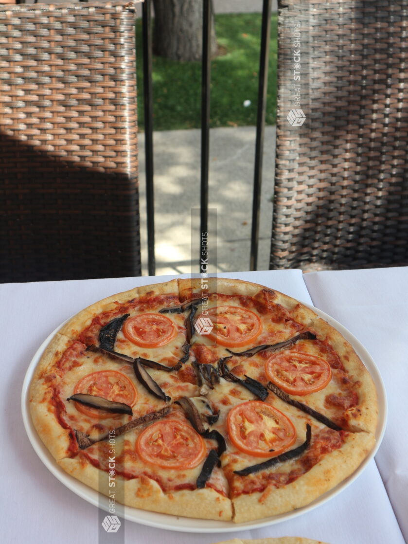 Medium tomato and portobello mushroom pizza on a white table cloth on an outdoor patio at a restaurant