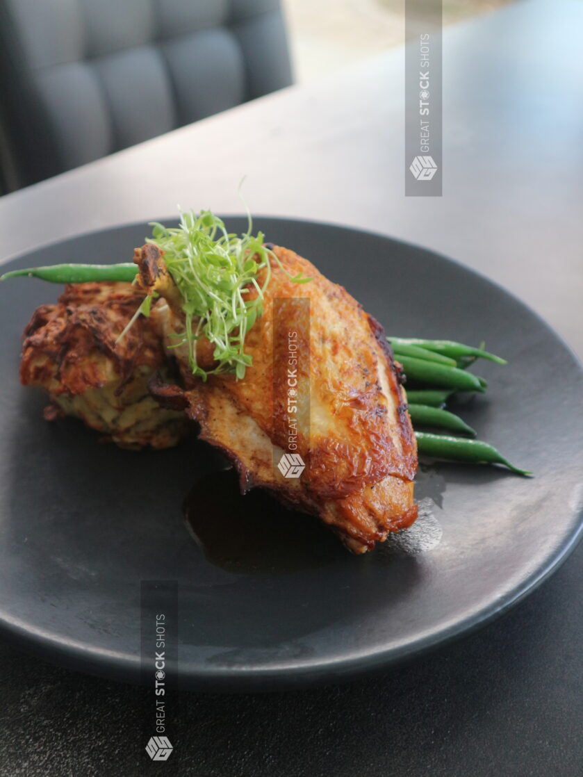 Oven roasted chicken breast with a side of green beans on a black plate