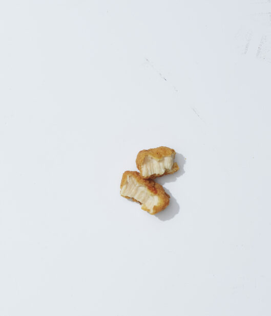 A single chicken nugget torn in half on a light background