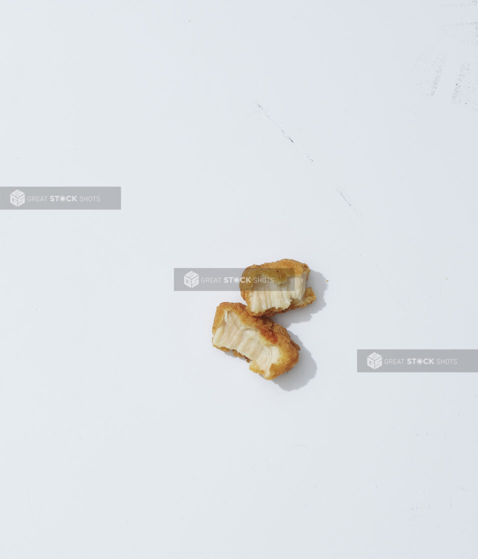 A single chicken nugget torn in half on a light background