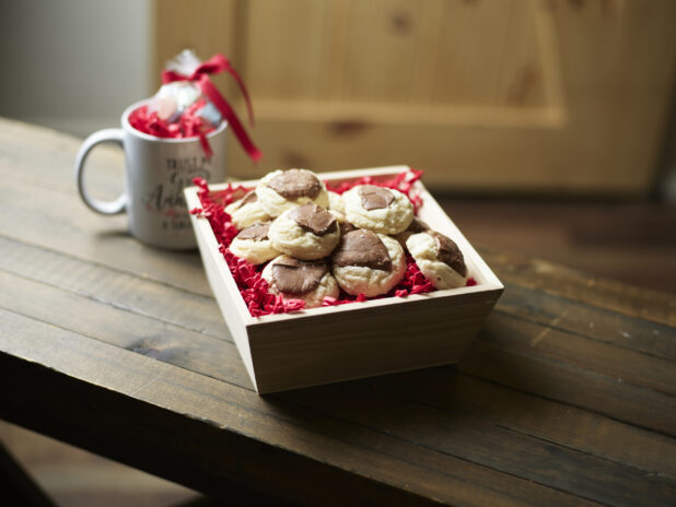 A Valentine's Day gift box with shortbread cookies chocolate and an accompanying mug on a dark wooden table