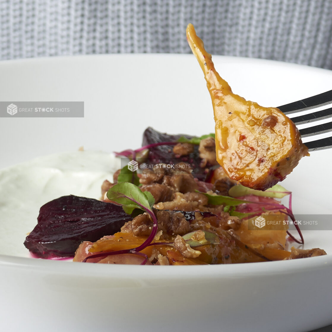 Roasted root vegetable salad with micro greens and nuts in a white bowl, close-up