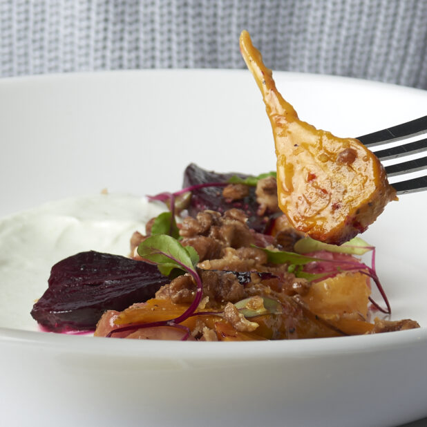 Roasted root vegetable salad with micro greens and nuts in a white bowl, close-up