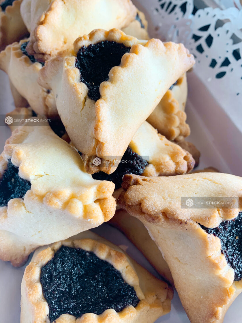 Close Up of Traditional Jewish Hamantaschen Pastries with Poppyseed Paste Filling on a Doily Lined Platter