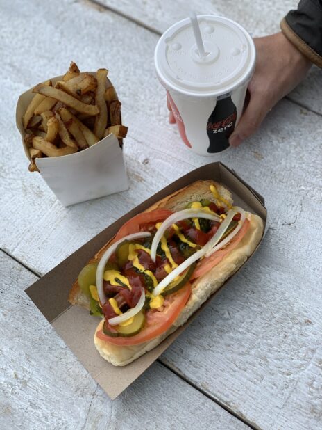 Combo with loaded hot dog, fresh cut french fries and a fountain drink on a wood table
