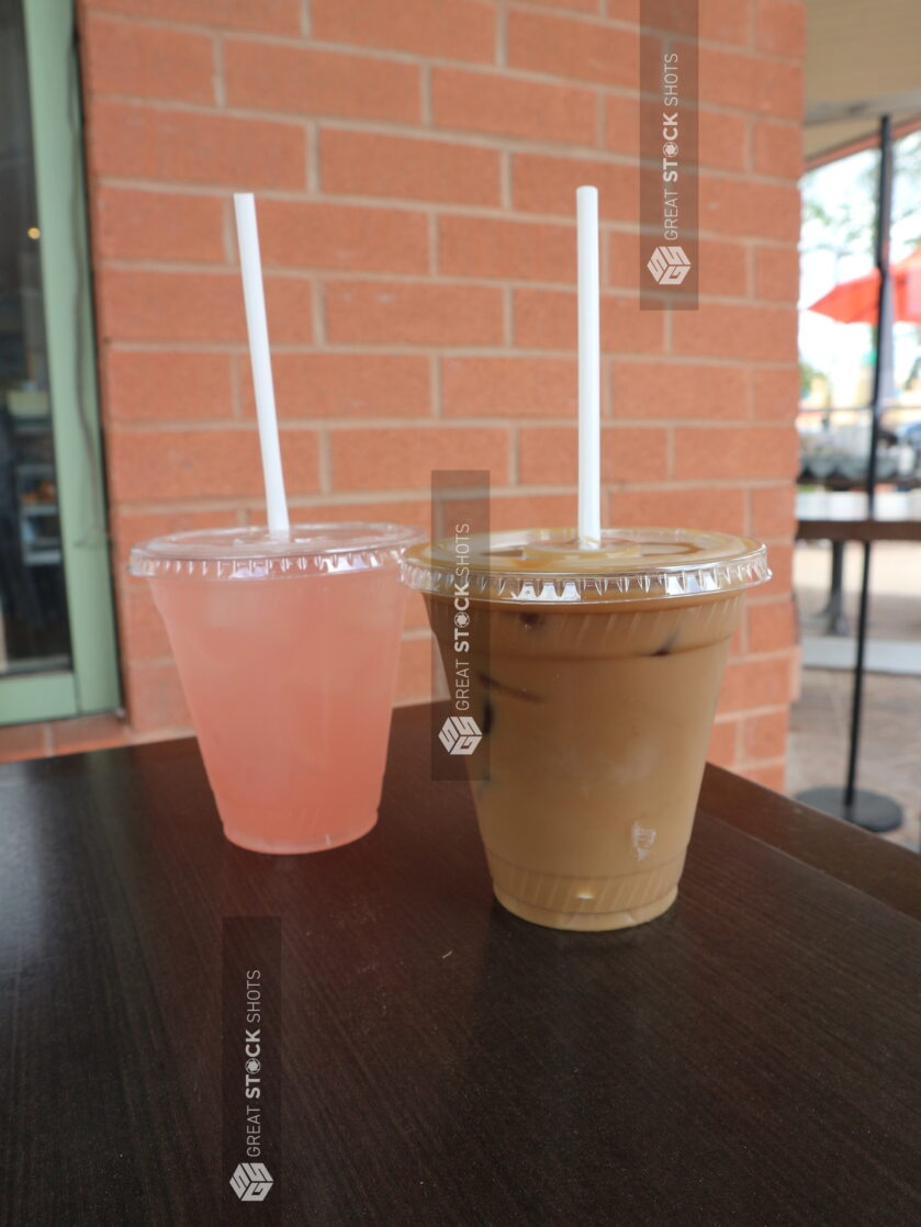 Two cold beverages with on a wooden table outside on a patio next to a brick wall