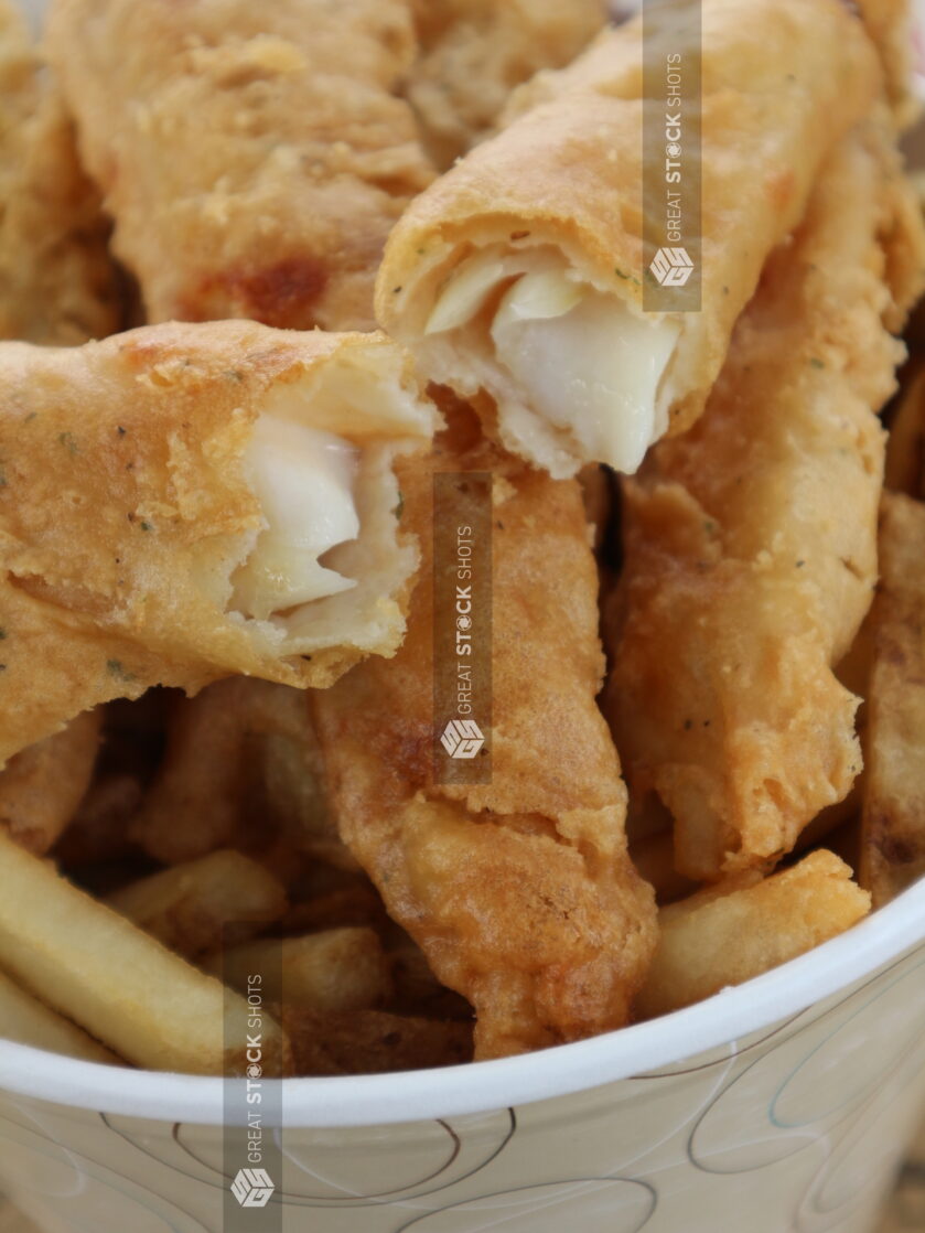 Close up of fish sticks with one broken in half on top of french fries in a disposable container