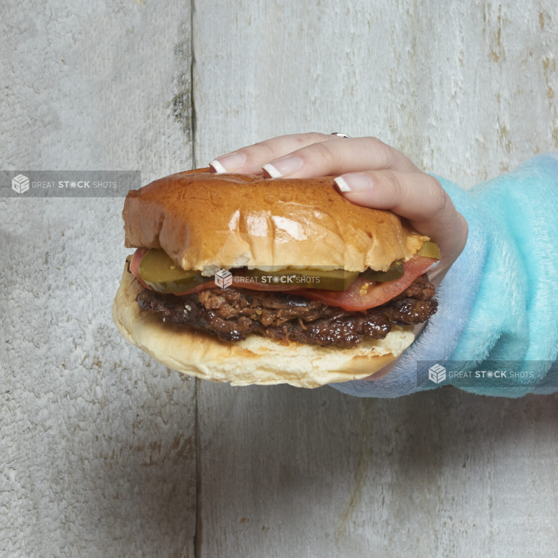 Hand holding a pulled pork sandwich with pickles and tomatoes with wooden background