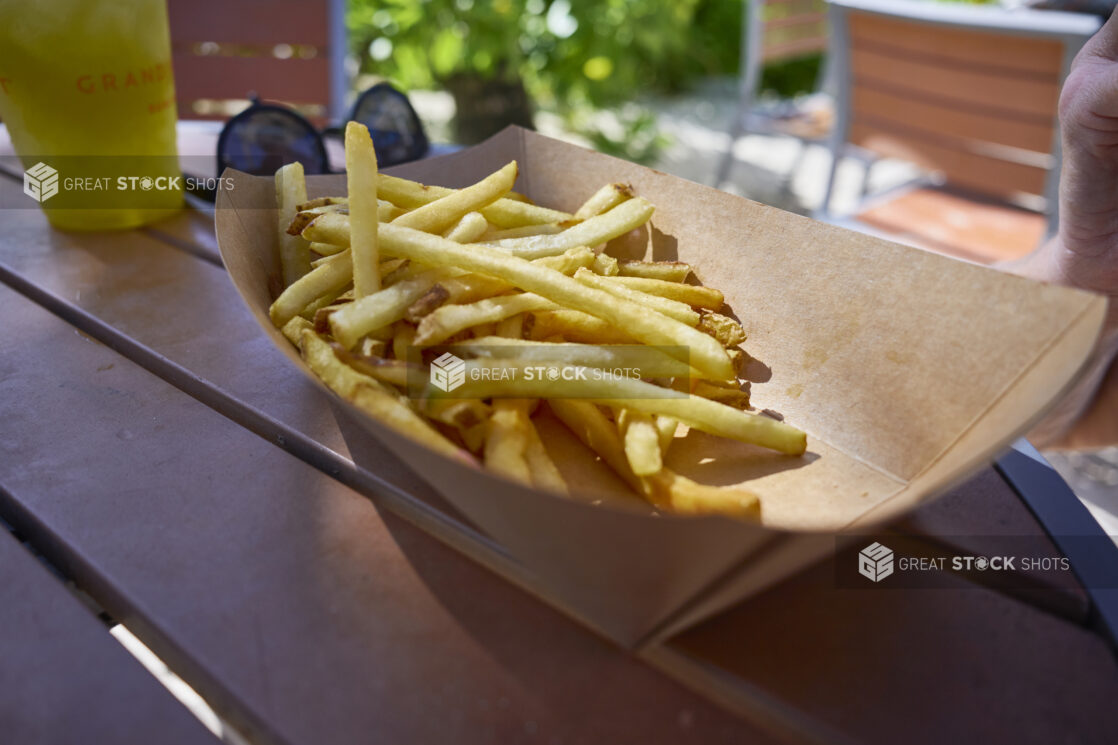 Close Up of Thin-Cut French Fries in a Paper Take-Out Container on a Patio Table
