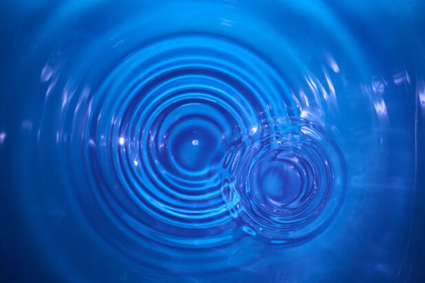 Overhead Close Up View of Water Droplets Creating Ripples in Clear Blue Water