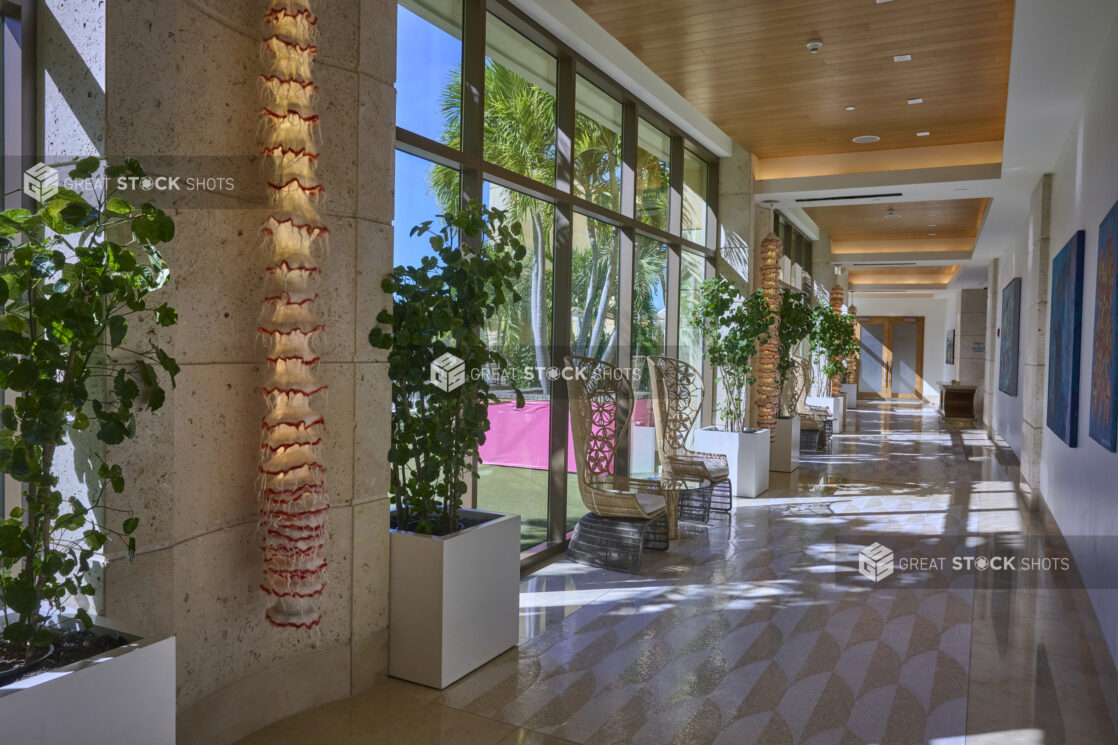 Outer Hallway of a Resort Hotel with Floor to Ceiling Windows, Potted Indoor Trees and Tall Back Wicker Chairs in Nassau, Bahamas