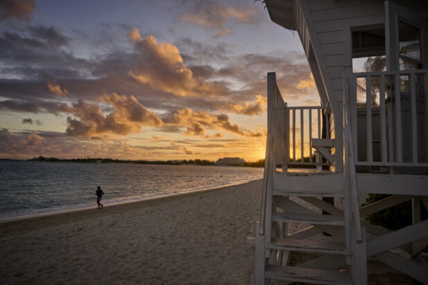 Landscape View of a Sandy Tropical Beach and Beach House at Sunset or Sunrise with a Silhouette of a Lone Jogger in Nassau, Bahamas