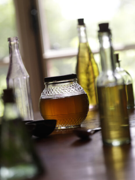 Close Up of a Jar of Honey with Other Glass Bottles of Oil on a Wooden Table in a Kitchen Setting