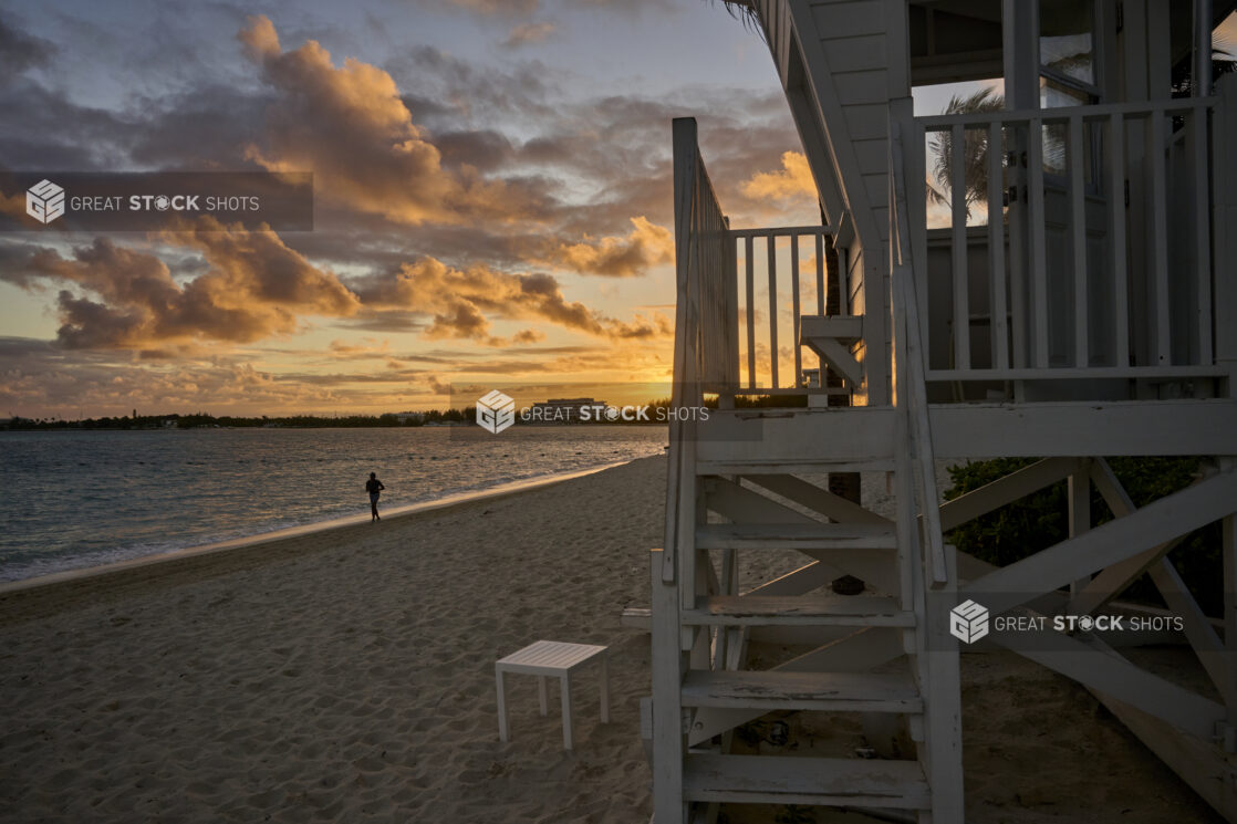 Landscape View of a Sandy Tropical Beach and Beach House at Sunset or Sunrise with a Silhouette of a Lone Jogger in Nassau, Bahamas - variation