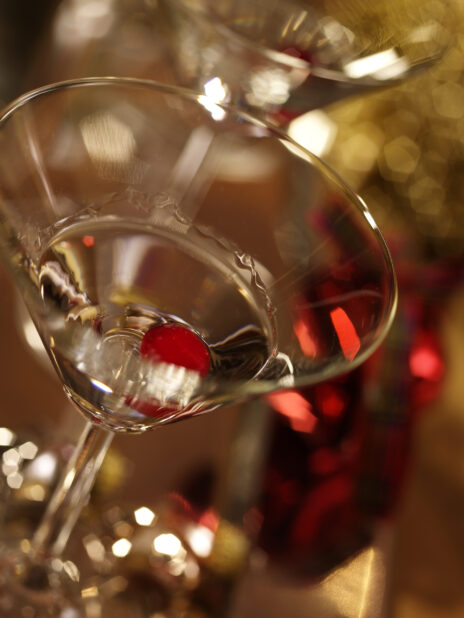 Close Up of Vodka and a Maraschino Cherry in a Martini Glass with a Heavy Bokeh Effect in the Background in an Indoor Setting