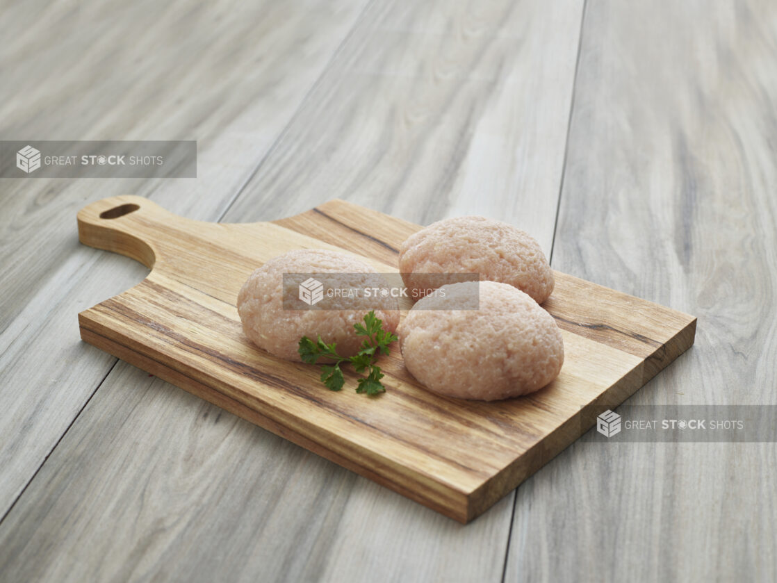 Three thick chicken burger patties on wood paddle