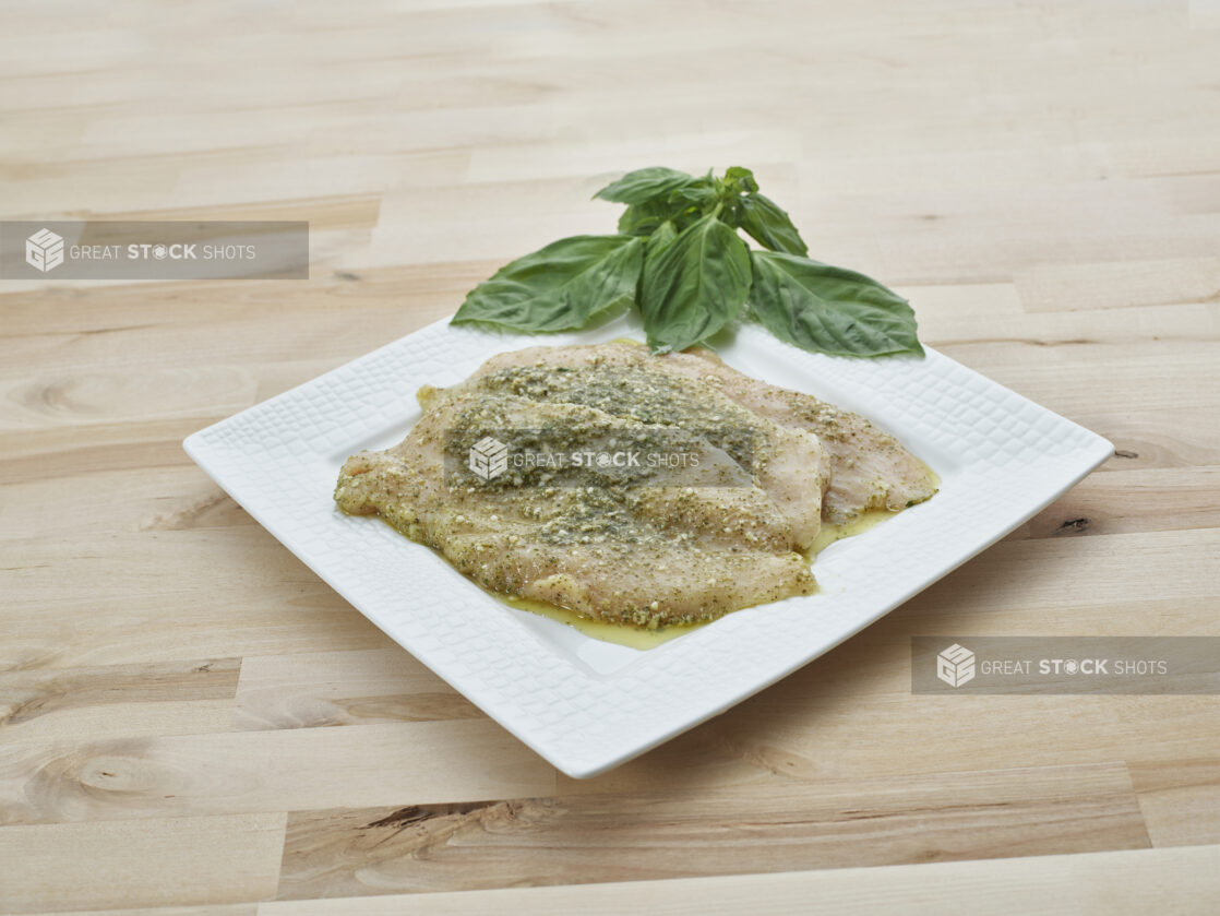 Pesto marinated seasoned chicken breast cutlets on a decorative square white plate