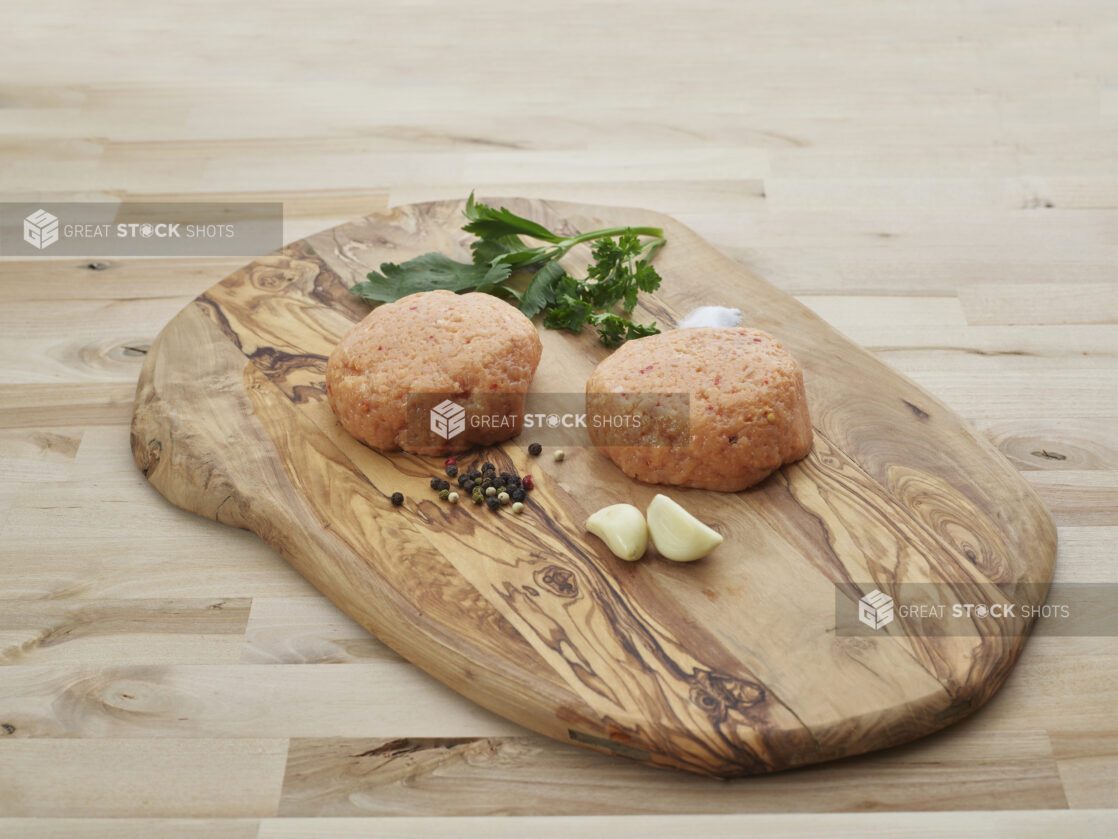 Two thick Buffalo chicken burger patties with seasonings on natural wood cutting board