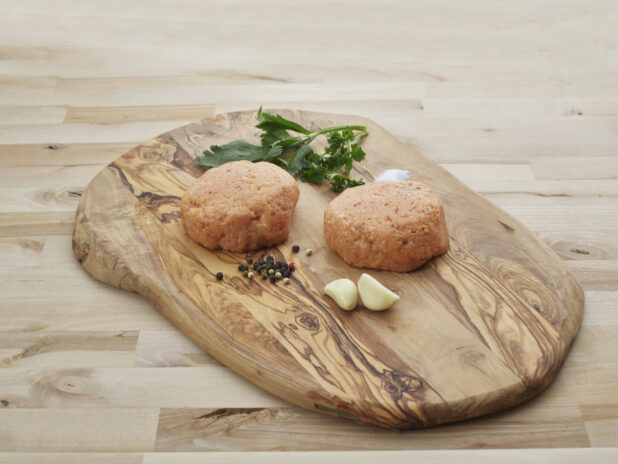 Two thick Buffalo chicken burger patties with seasonings on natural wood cutting board