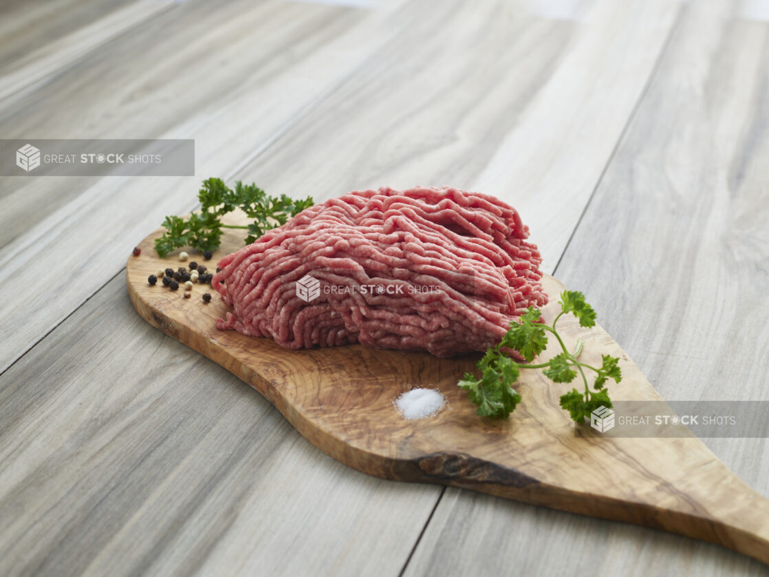 Raw ground beef with seasonings on a wooden board, close-up