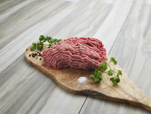 Raw ground beef with seasonings on a wooden board, close-up