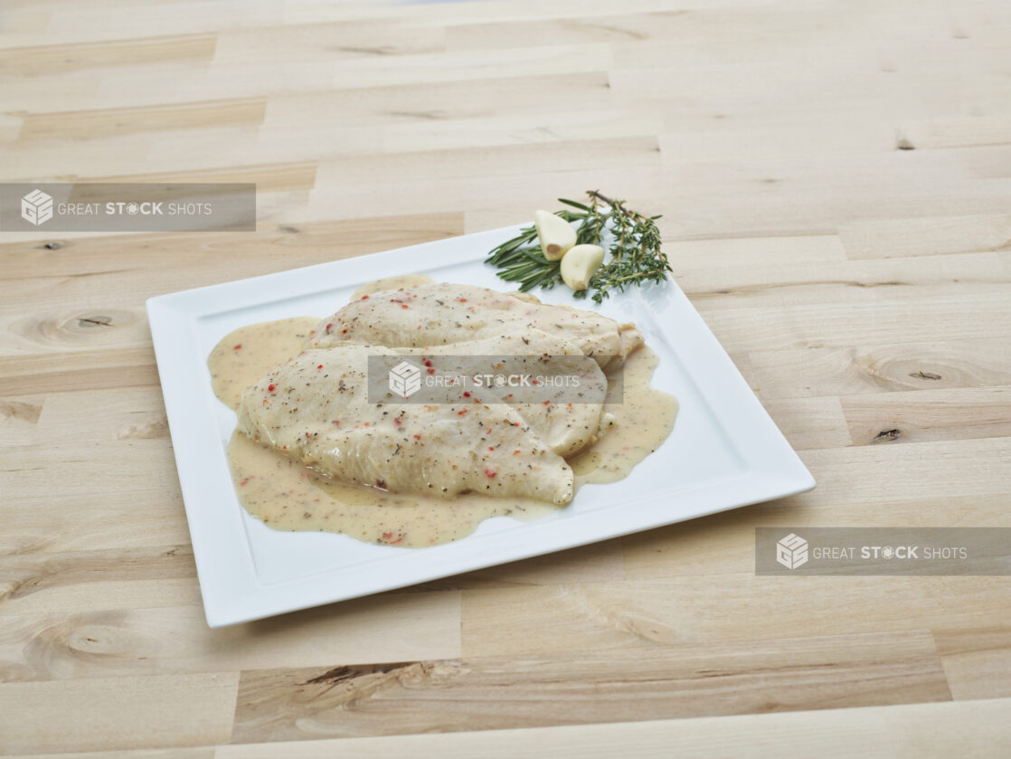 Marinated herb and garlic chicken breast cutlets on a decorative square white plate