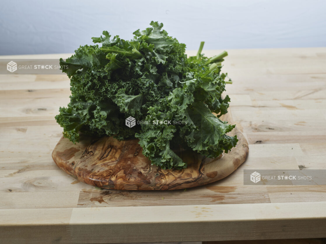 Fresh curly kale piled on a round natural wood board, close-up