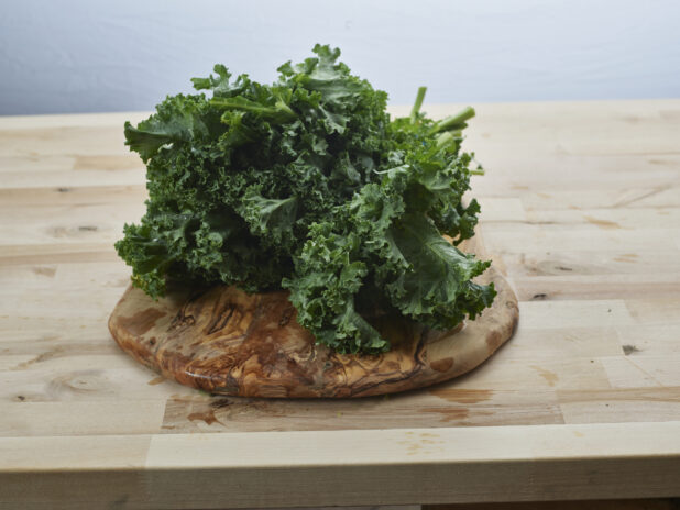 Fresh curly kale piled on a round natural wood board, close-up