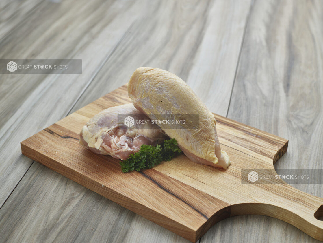 Whole raw chicken breast with skin and bones, split in two on a wood paddle, close-up