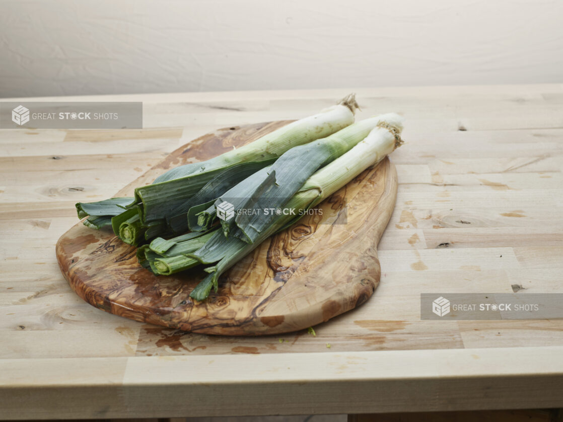 Three whole leeks on a natural wood board, close-up