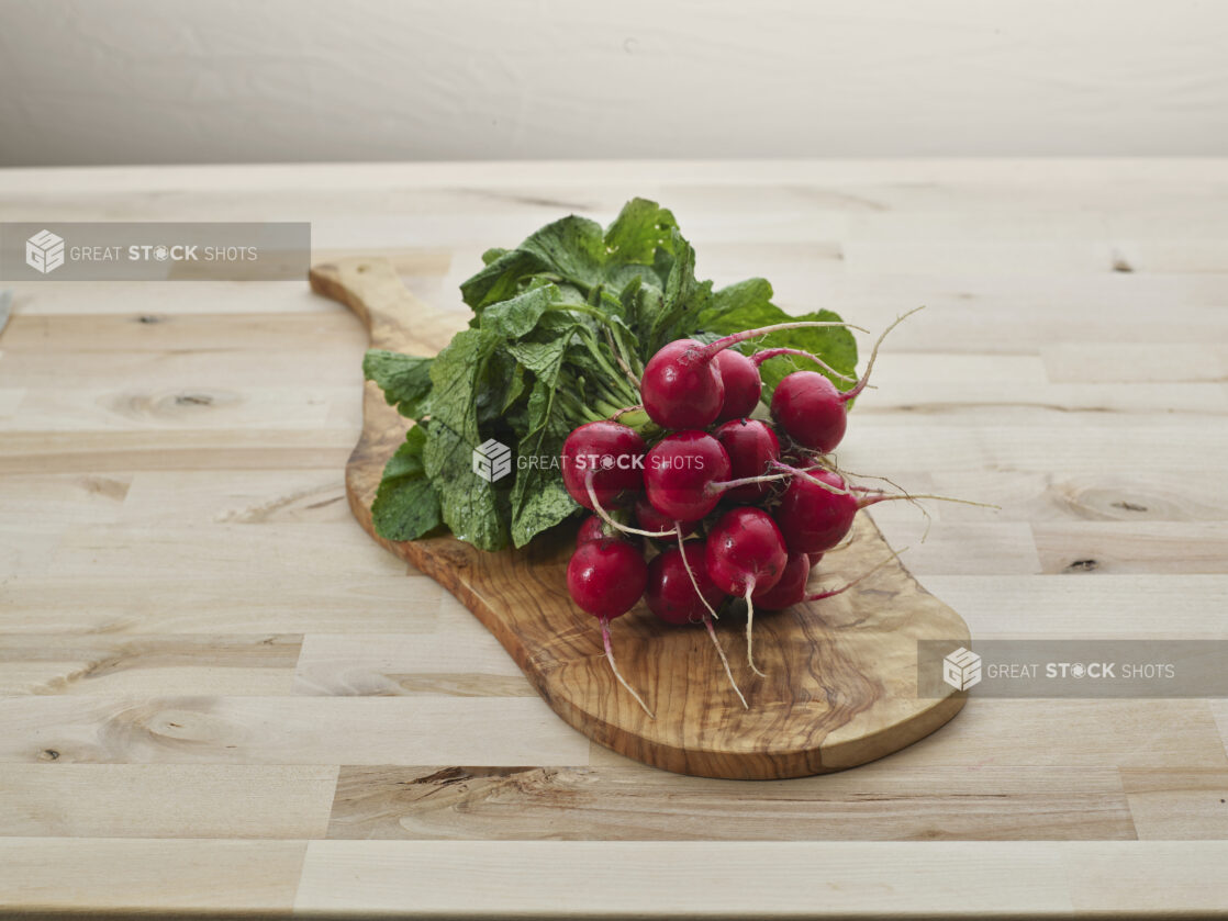 Bunch of fresh radishes on a natural wood paddle, close-up