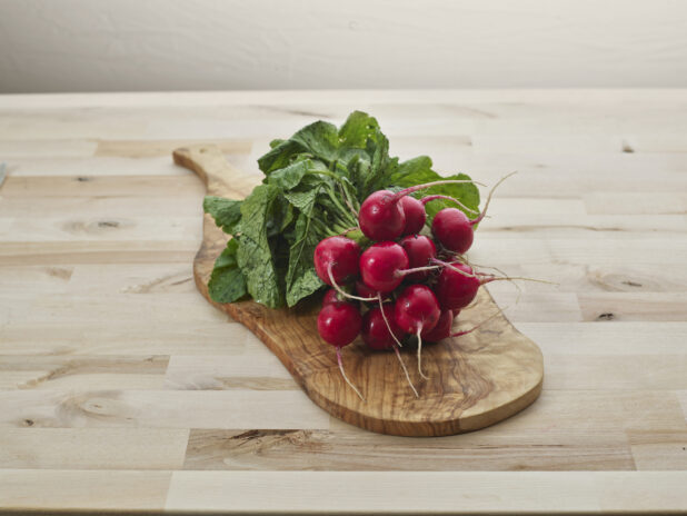 Bunch of fresh radishes on a natural wood paddle, close-up