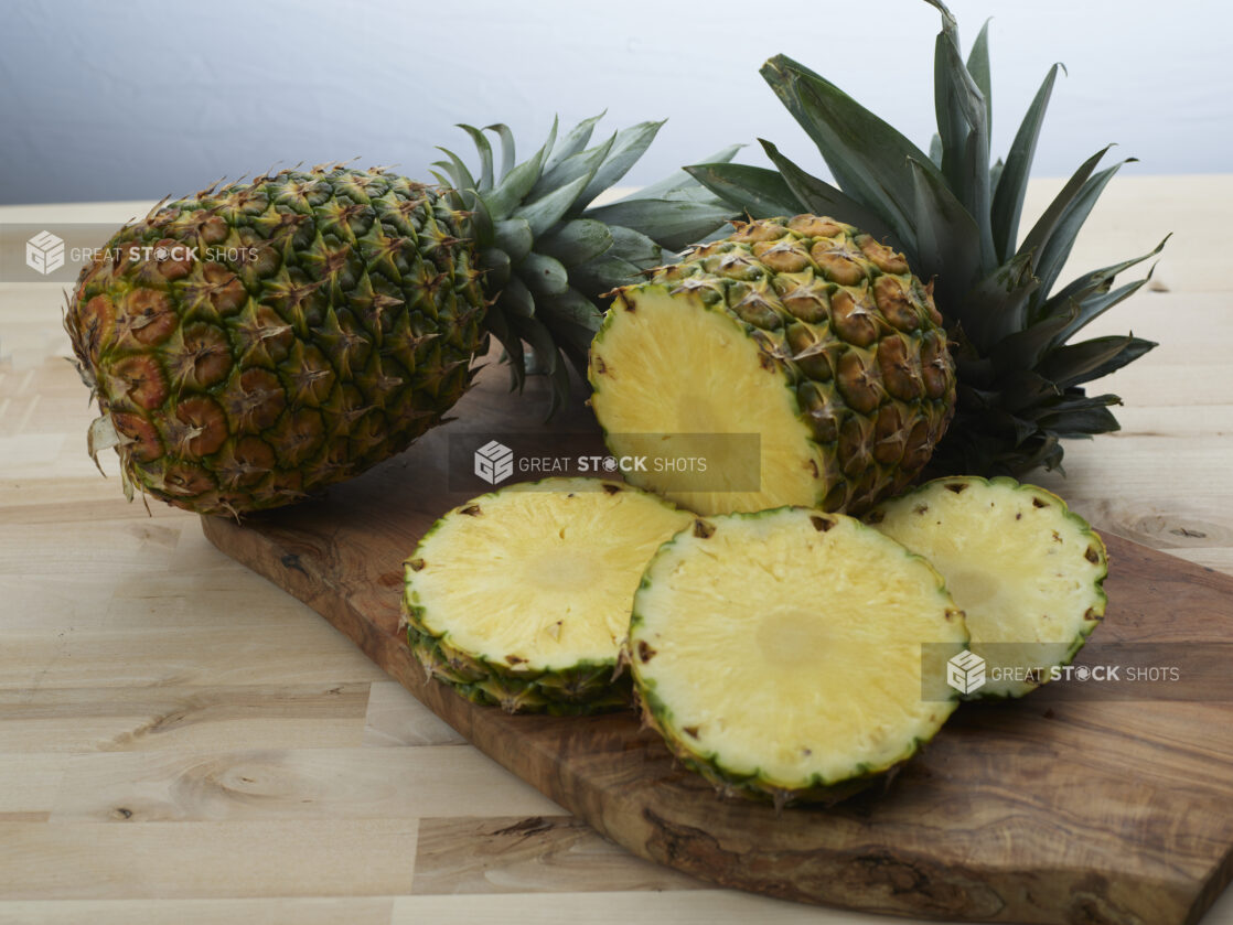 Fresh pineapples, whole and sliced, on a wooden board, close-up