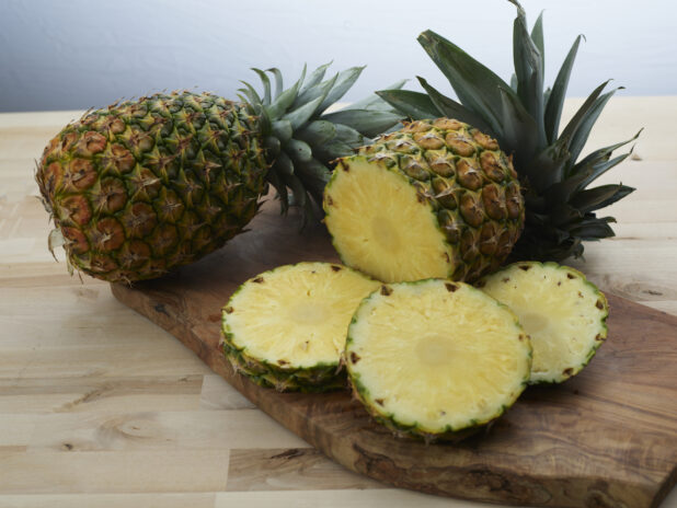 Fresh pineapples, whole and sliced, on a wooden board, close-up