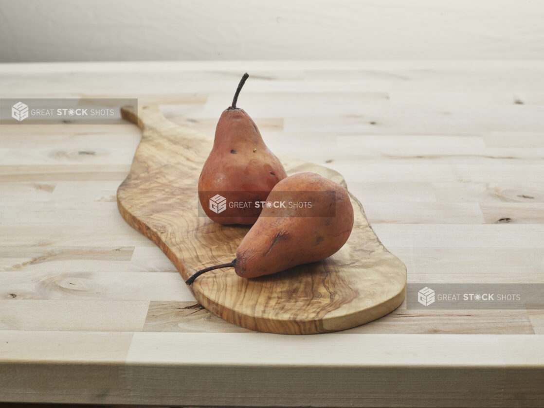 Two Bosc pears on a natural wood paddle, close-up