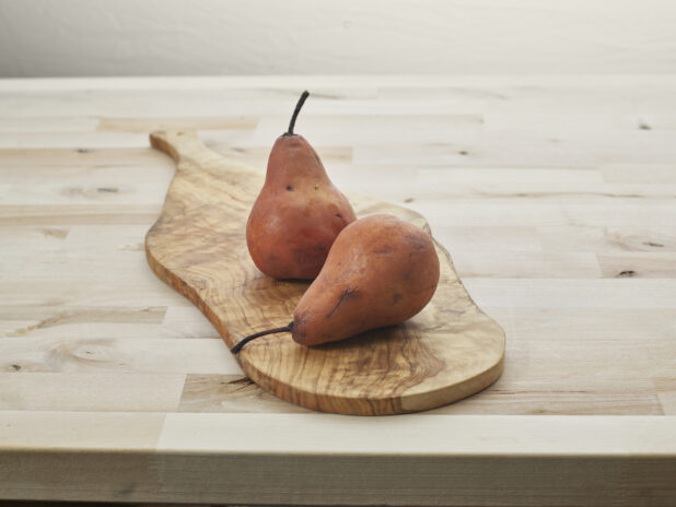 Two Bosc pears on a natural wood paddle, close-up