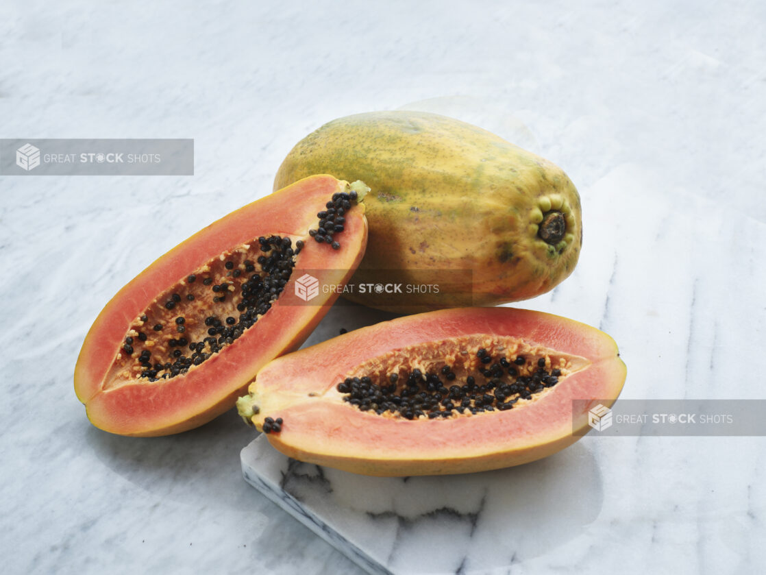 Papayas, whole and halved, on white marble board, close-up, marble background