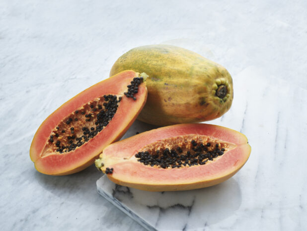 Papayas, whole and halved, on white marble board, close-up, marble background