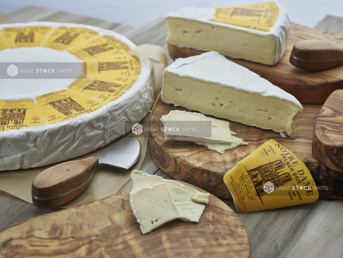 French brie in wheel, wedges, and slices on natural wood boards, close-up