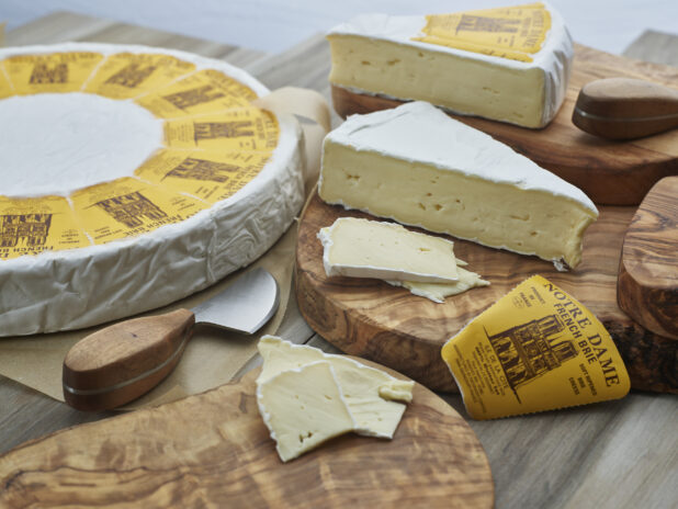 French brie in wheel, wedges, and slices on natural wood boards, close-up