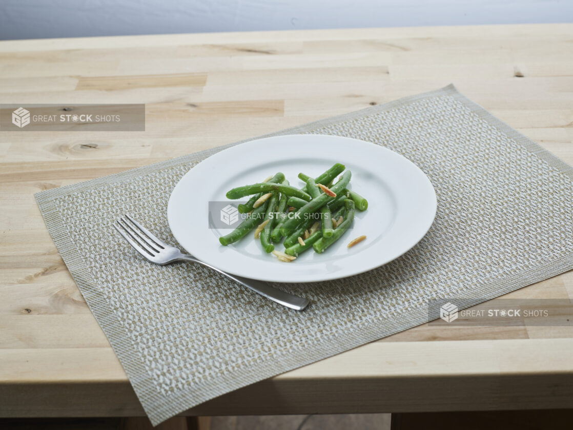 Green beans with slivered almonds on a white plate, woven placemat