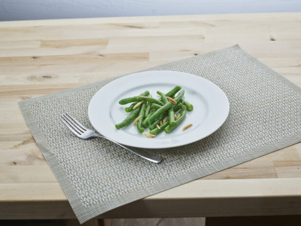 Green beans with slivered almonds on a white plate, woven placemat