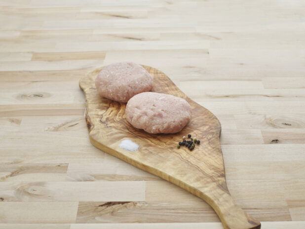 Two thick turkey burger patties on wood paddle
