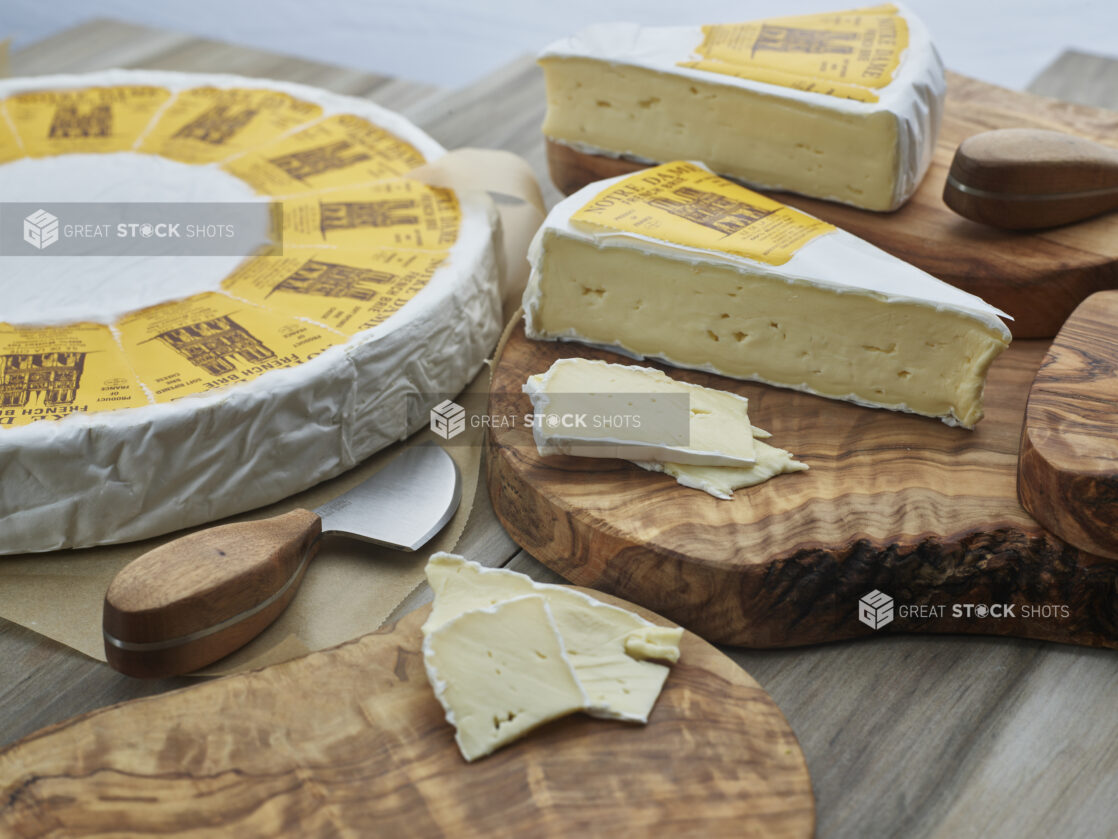 French brie in wheel, wedges, and slices on natural wood boards, close-up