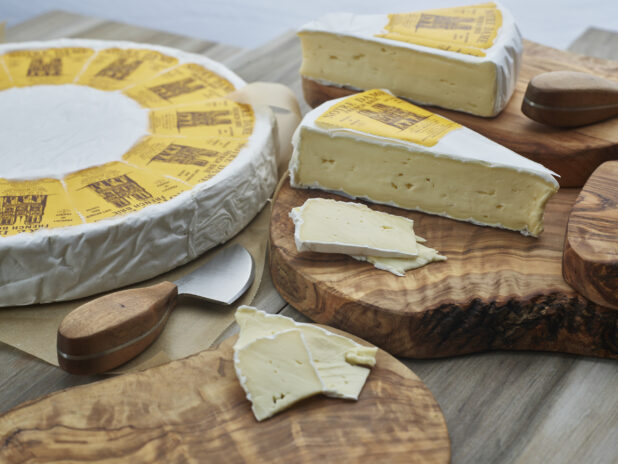 French brie in wheel, wedges, and slices on natural wood boards, close-up